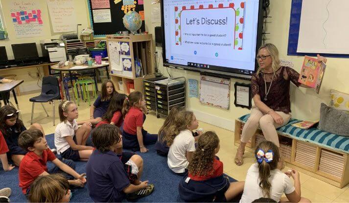 Teacher leading a lesson for young students seated on the classroom floor
