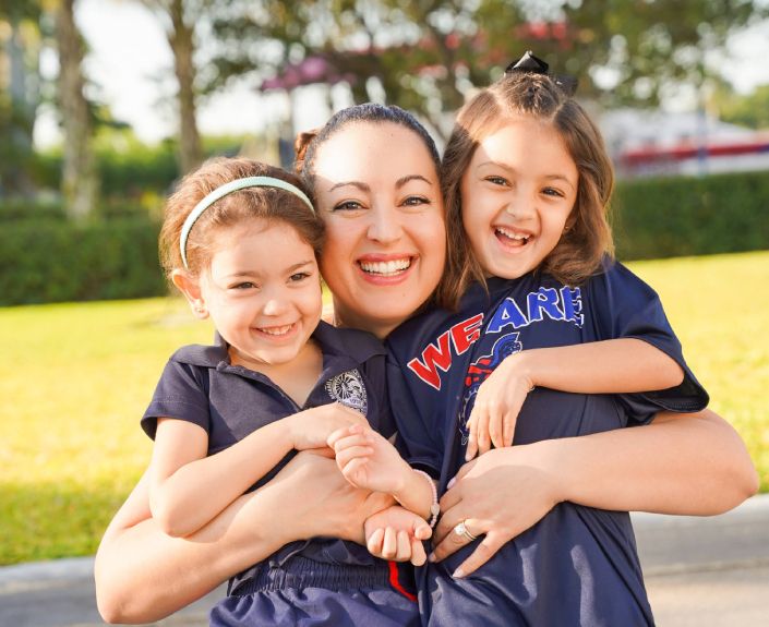 Mother smiling and embracing her two daughters in school uniforms outdoors