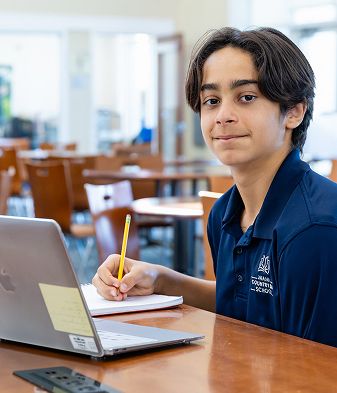 Upper School student taking notes beside a laptop