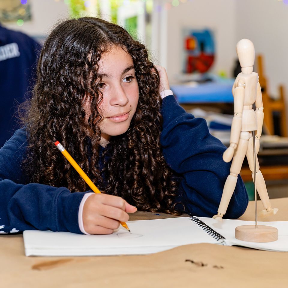 Visual Arts student sketching beside a wooden artist mannequin