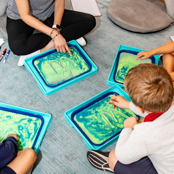 Early Childhood students playing with sensory sand trays on the floor