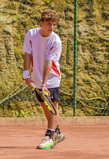 Teen tennis player in white shirt and black shorts preparing to hit a backhand on a clay court