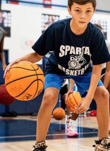 Boy in a Sparta Basketball t-shirt dribbling a basketball on an indoor court