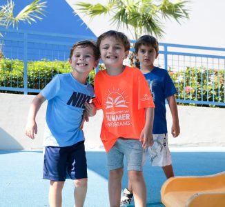 Three young boys smiling together on a playground at Miami Country Day Summer Programs