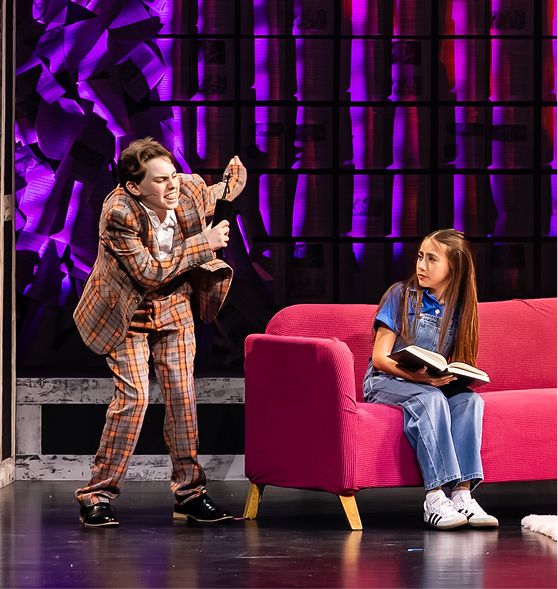 Two MCDS Theater students performing a scene with one seated on a sofa