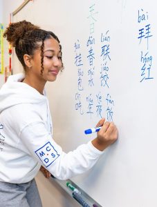 Student writing Chinese characters on a whiteboard in language class