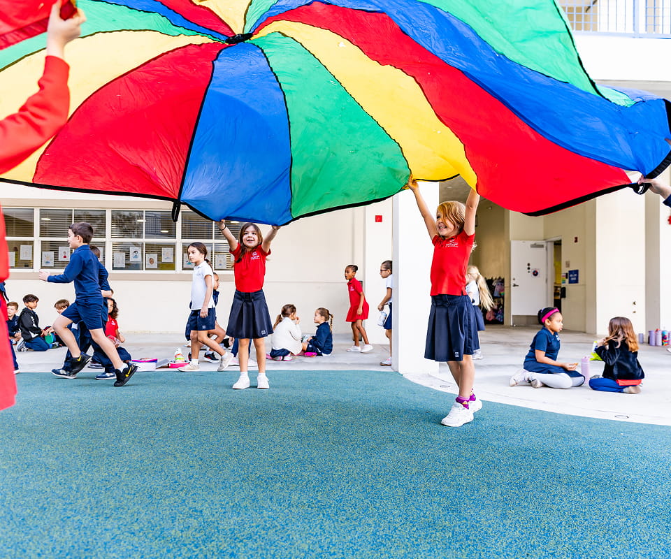 Elementary students in school uniforms playing with a colorful parachute during outdoor recess