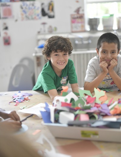 Two MCDS summer camp students smiling while creating a paper craft project in art class