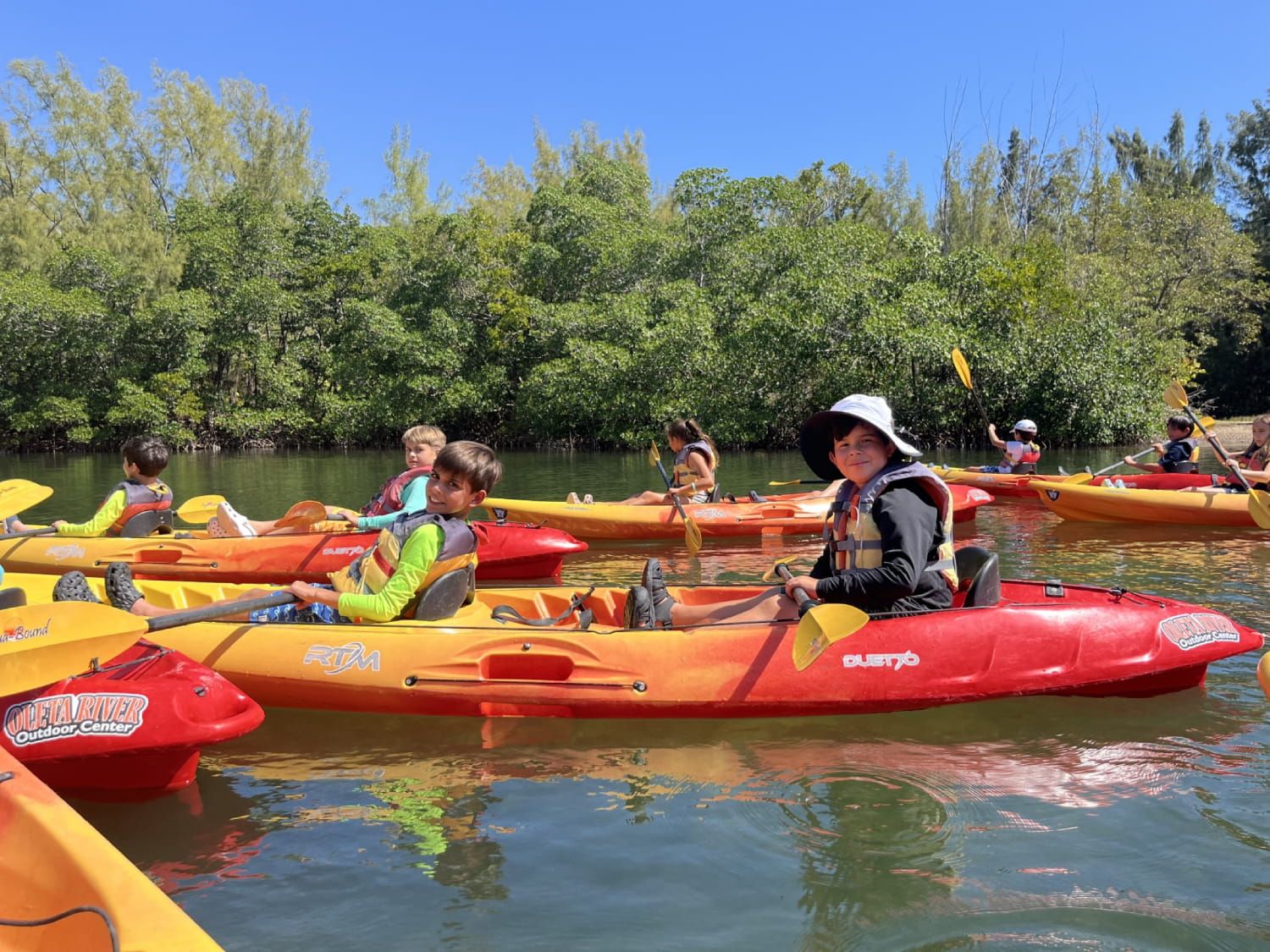 Students in life jackets kayaking together on a river surrounded by mangroves