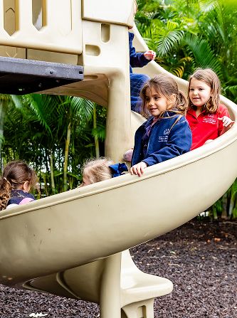 Young MCDS students playing on a playground slide outdoors