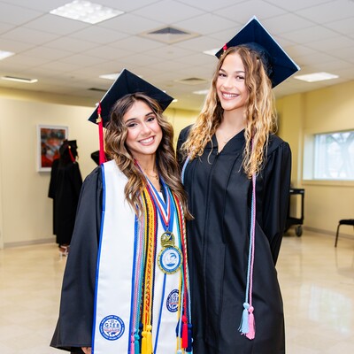 Two graduates in caps and gowns posing together after Commencement