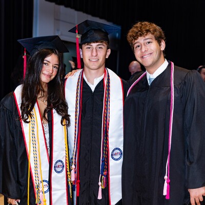 Three graduates in caps and gowns posing together after Commencement
