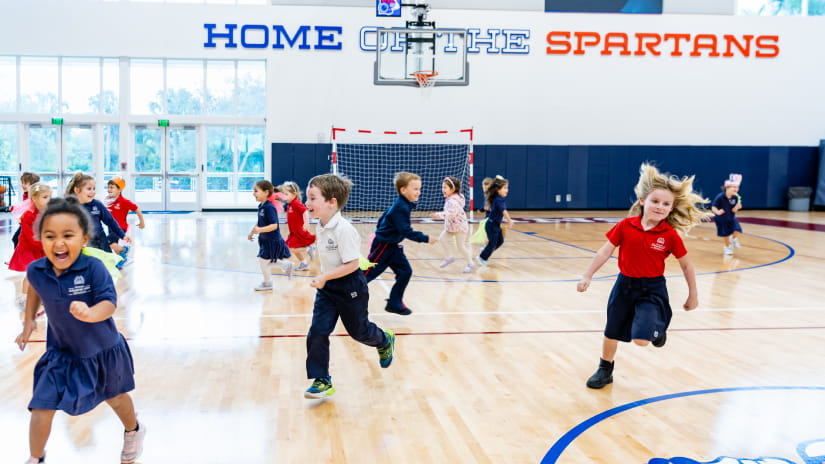 Young students running and laughing during a physical education class in the Spartans gymnasium