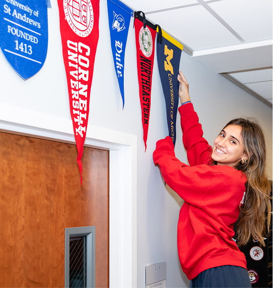 Student hanging university pennants on a College Counseling office wall