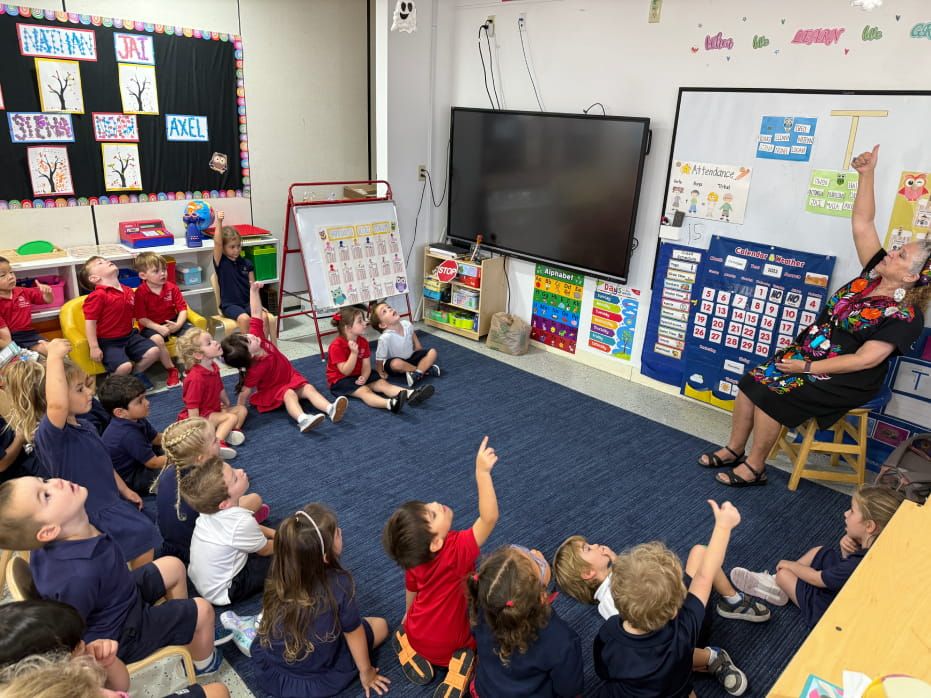 Senior kindergarten students sitting on a rug during circle time as their teacher points to a lesson board