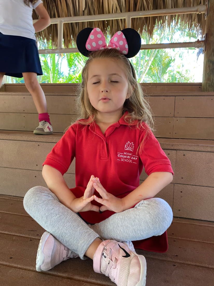 Young student in a red school polo sitting cross-legged with eyes closed during an outdoor yoga session