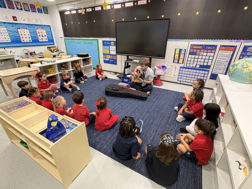 Teacher playing guitar for young students seated in a circle during music class