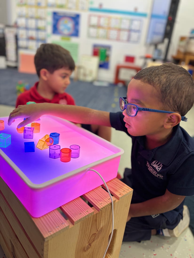 Young student exploring colorful shapes on a glowing light table in the classroom